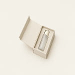 An open cream gift box holds an unmarked cosmetics bottle in a precisely fitted insert.