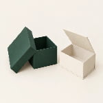 A forest-green lid-and-base gift box stands beside a cream book-style box with crisp wrapped corners.