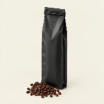 A matte black laminated side gusset coffee bag with a tin tie and centered degassing valve beside roasted coffee beans