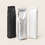Three side gusset coffee bags in matte black, metallic silver foil and matte white laminate, one with a tin tie and one with a degassing valve